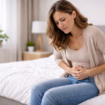 femeie cu disconfort abdominal într-un dormitor luminos